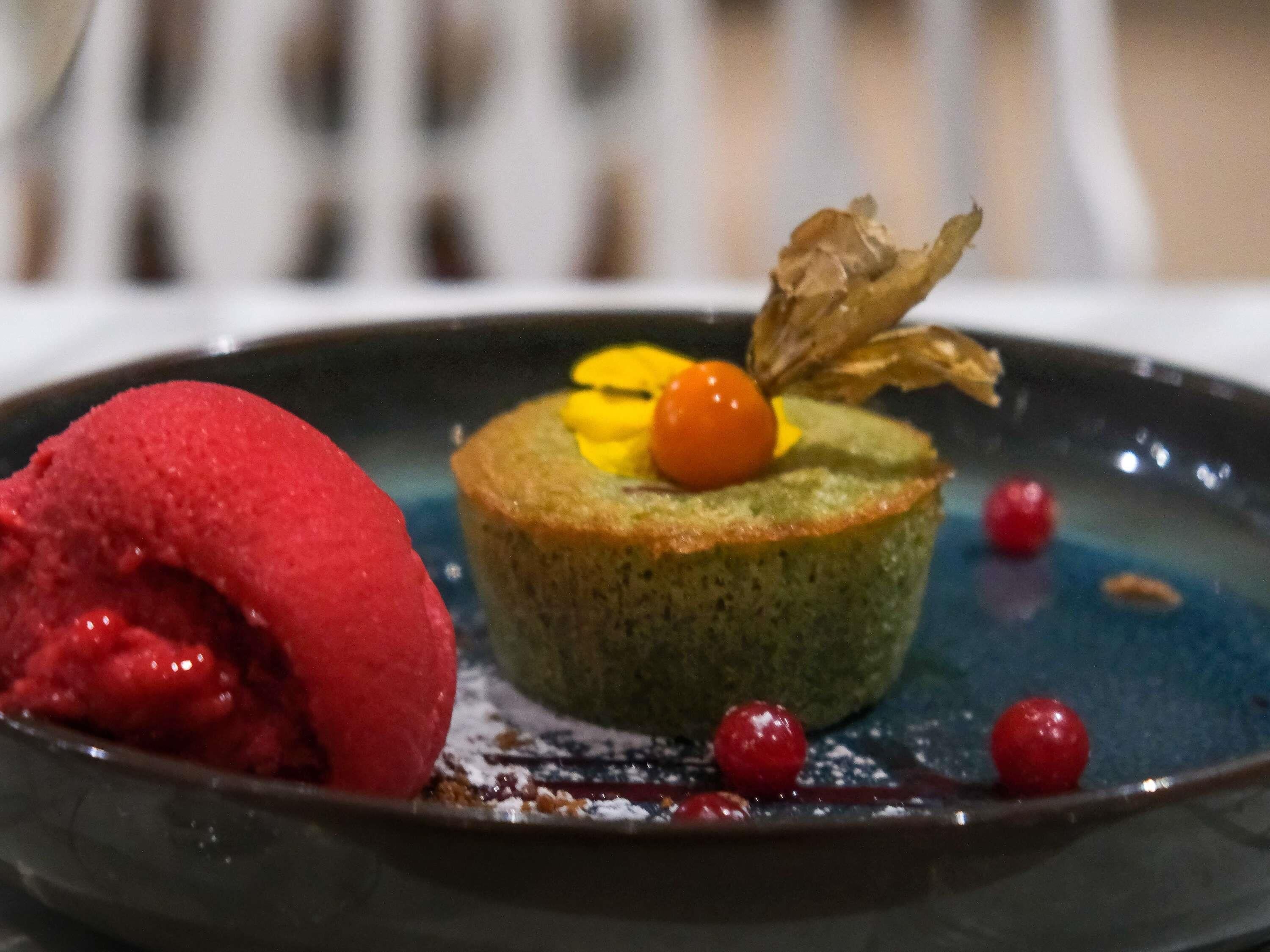 A dessert with a green base, a red scoop, and a cherry on top.