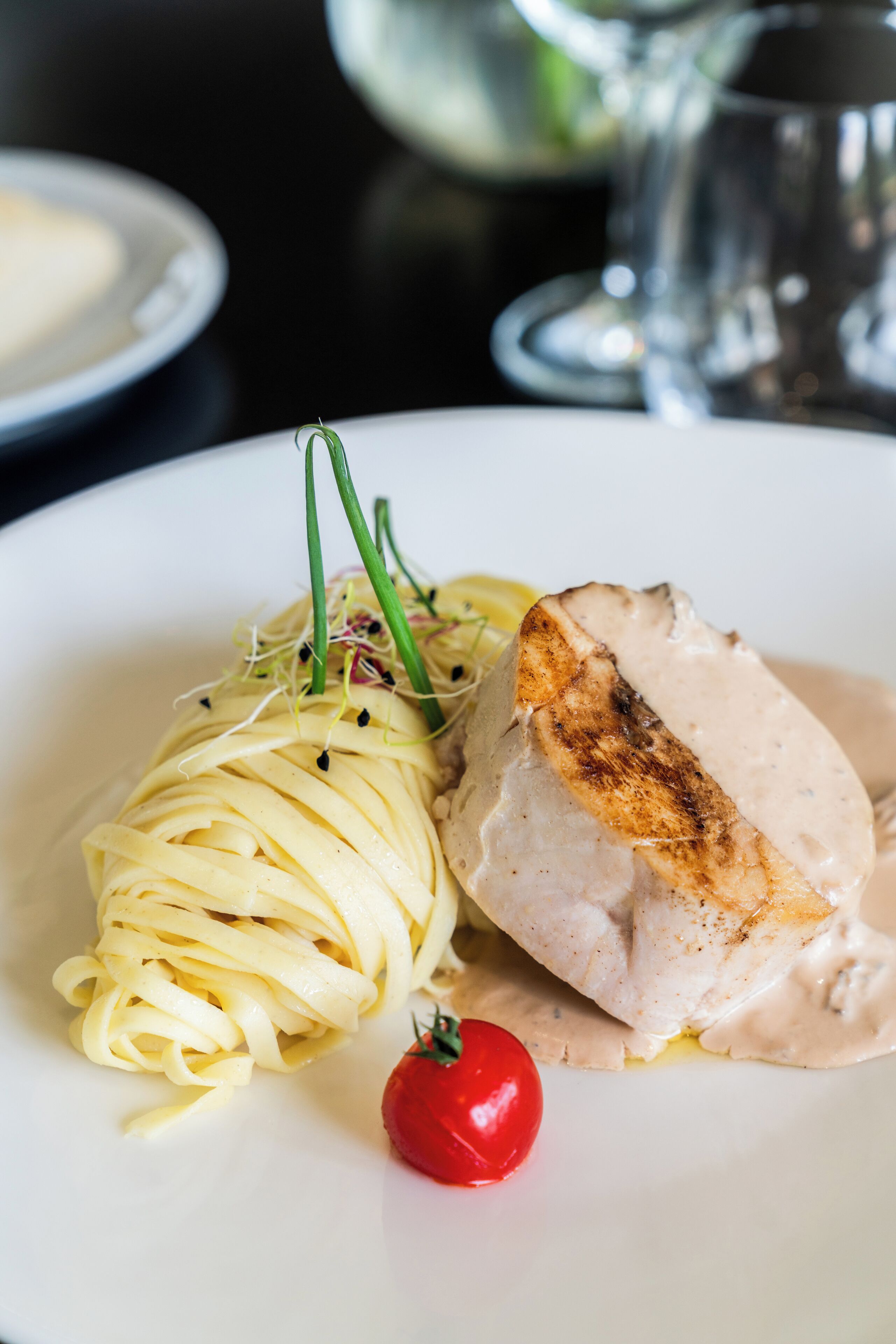 Un plato de pasta con pechuga de pollo a la parrilla y tomate cherry.