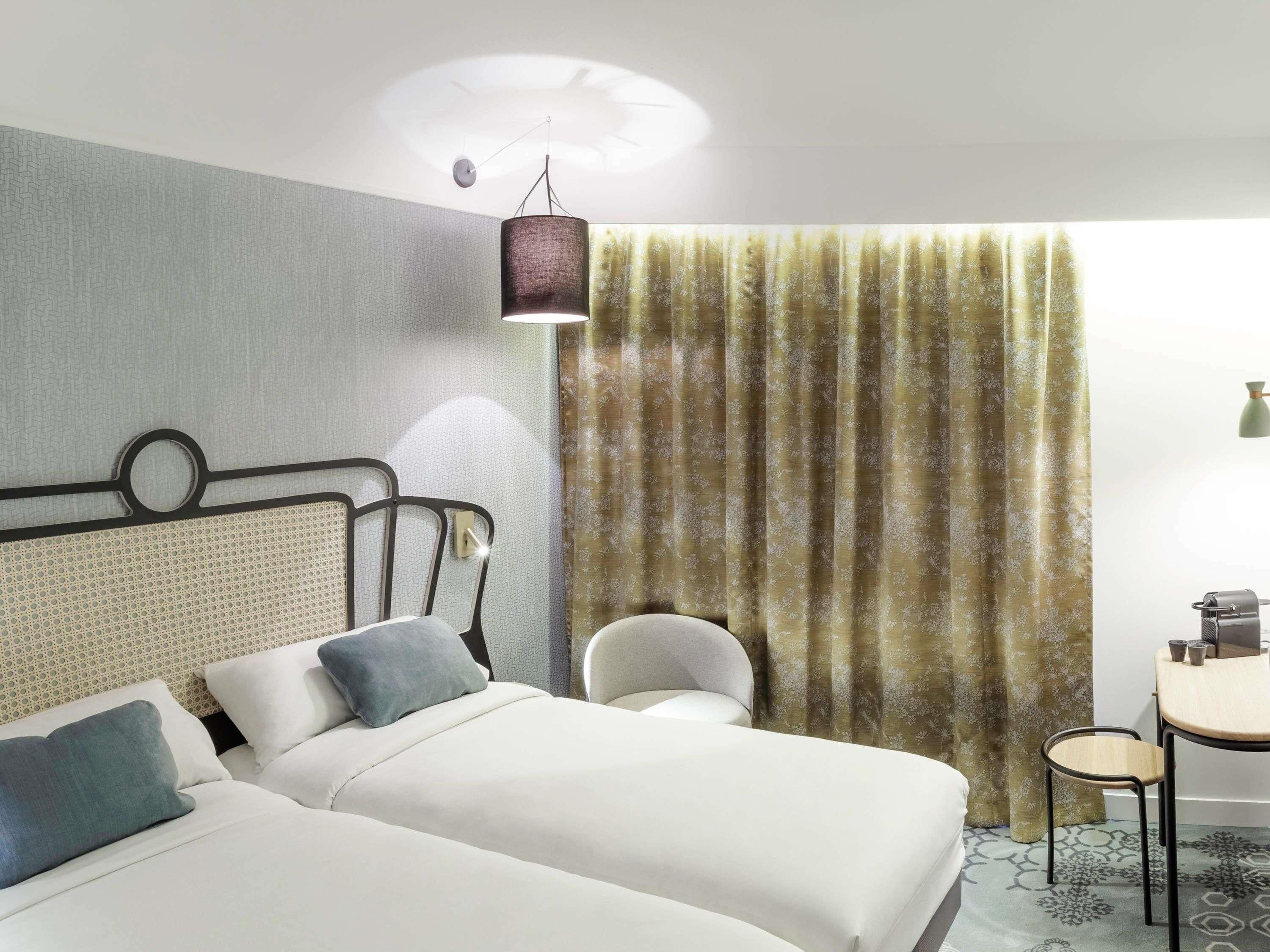 A hotel room with two beds, a desk, a chair, and a window with curtains.