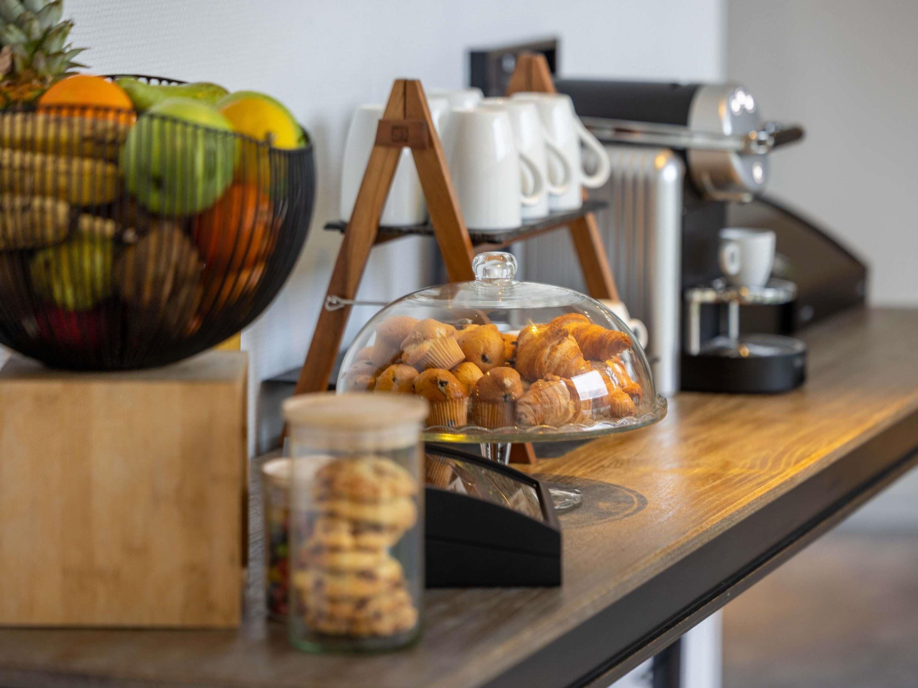 A breakfast setup with pastries, a fruit bowl, and coffee-making equipment.