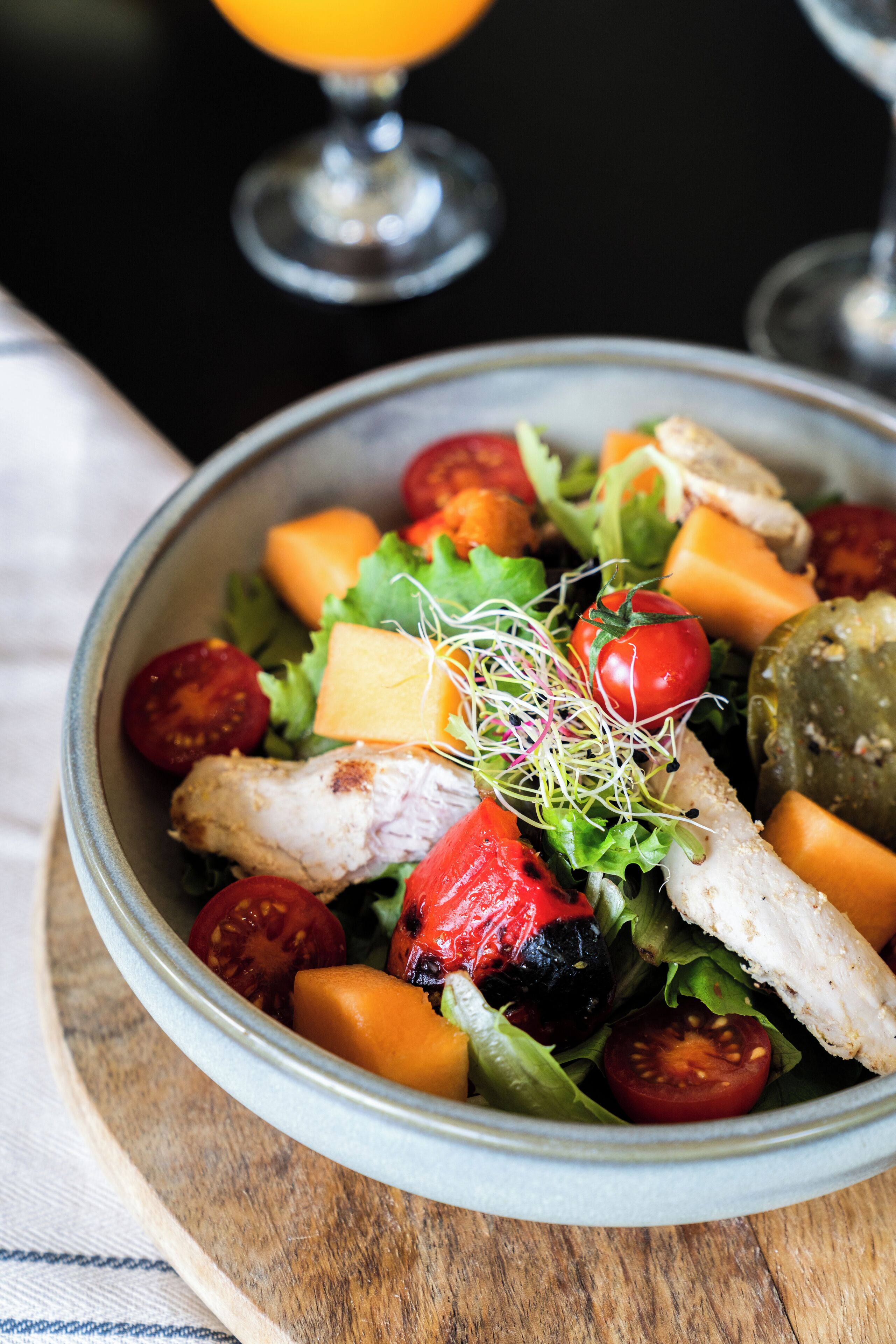 A bowl of salad with various vegetables and a piece of chicken.