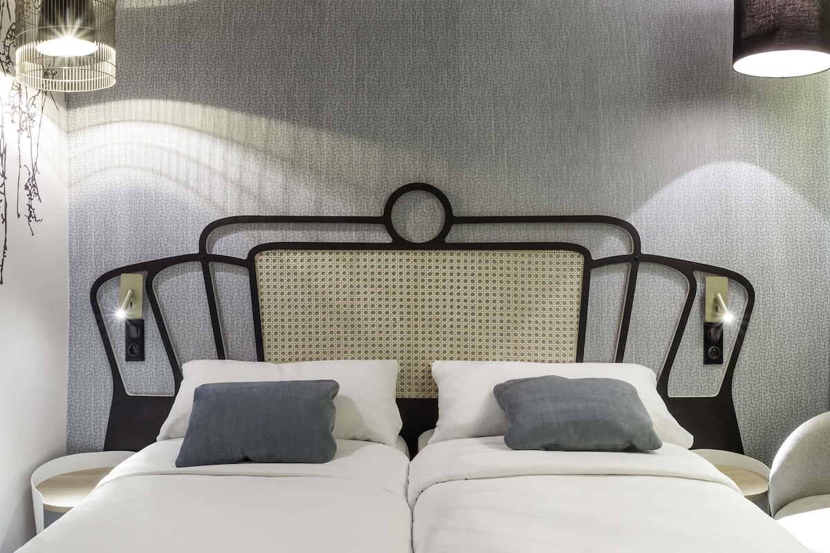 Uma cama de casal com cabeceira, duas mesas de cabeceira com abajures e uma parede com padrão geométrico.