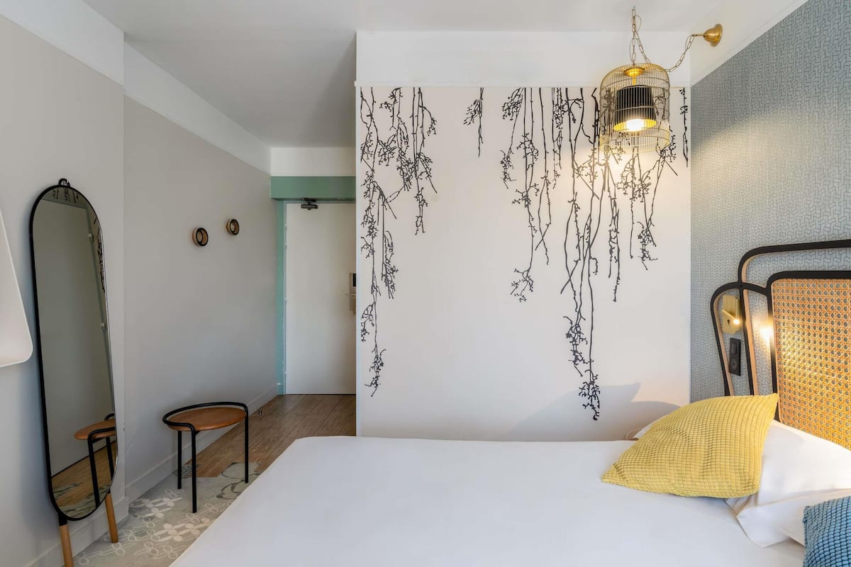 Quarto com cama, luminária pendente, espelho e parede com design de planta suspensa.
