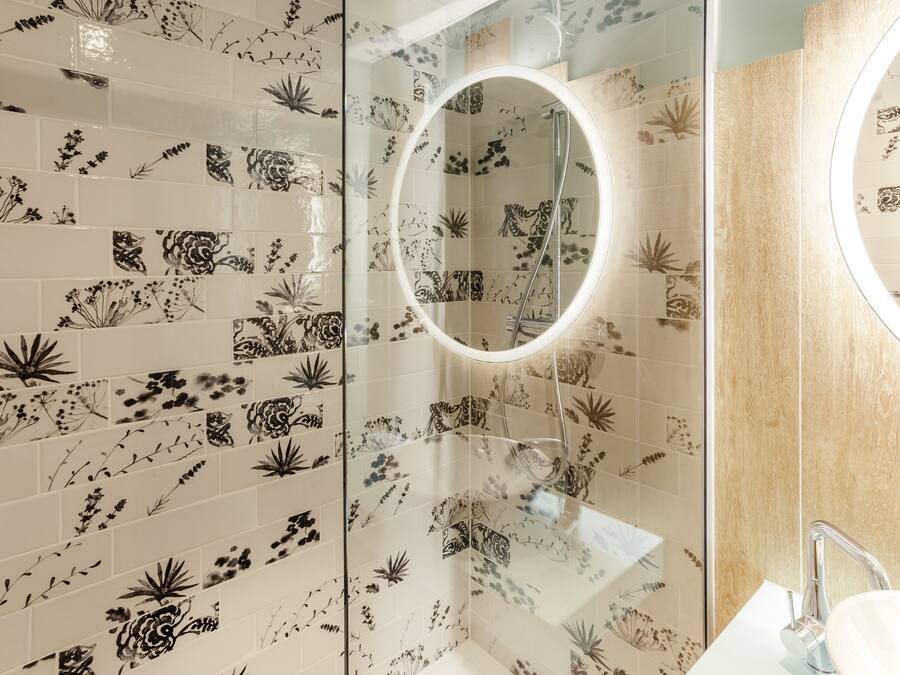 A bathroom with floral tile patterns, a glass shower enclosure, and a round mirror.