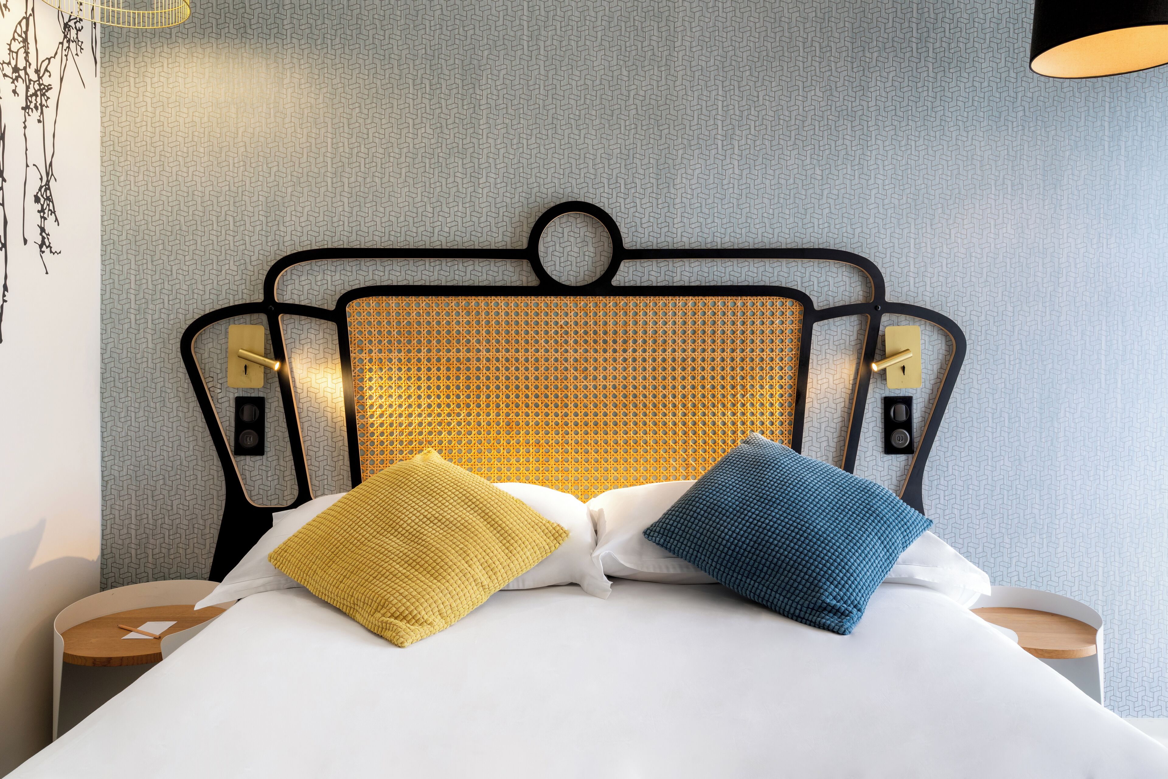 A neatly made bed with two pillows, a headboard with a geometric pattern, and a wall with a herringbone design.