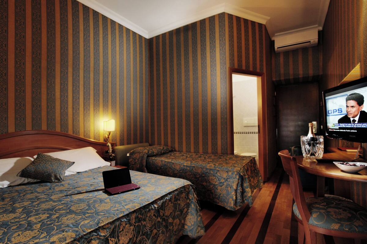Habitación de hotel con dos camas, un escritorio con una computadora portátil, un televisor y una zona de comedor.
