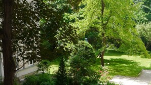 A pathway through a lush garden with various trees and shrubs, leading to a building with a white facade. - Astrid Hotel am Kurfürstendamm (Berlin)