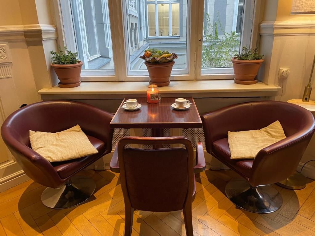 A dining area with two leather chairs, a small table, and a window with potted plants.