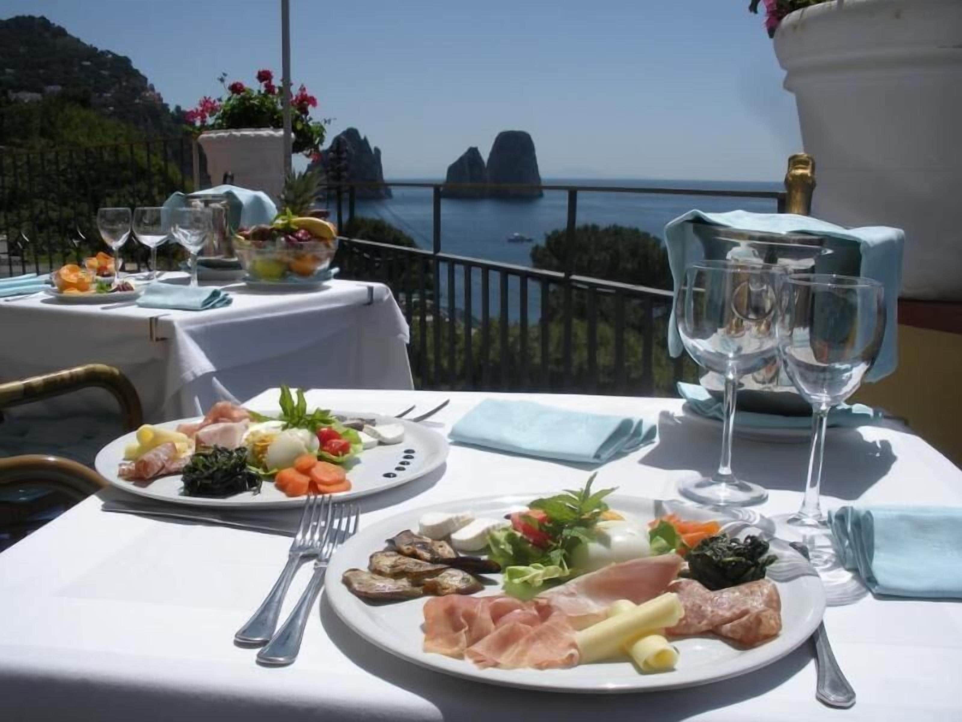 A table set for two with plates of food, wine glasses, and a view of the sea.