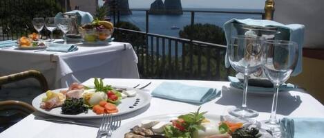 A table set for two with plates of food, wine glasses, and a view of the sea.