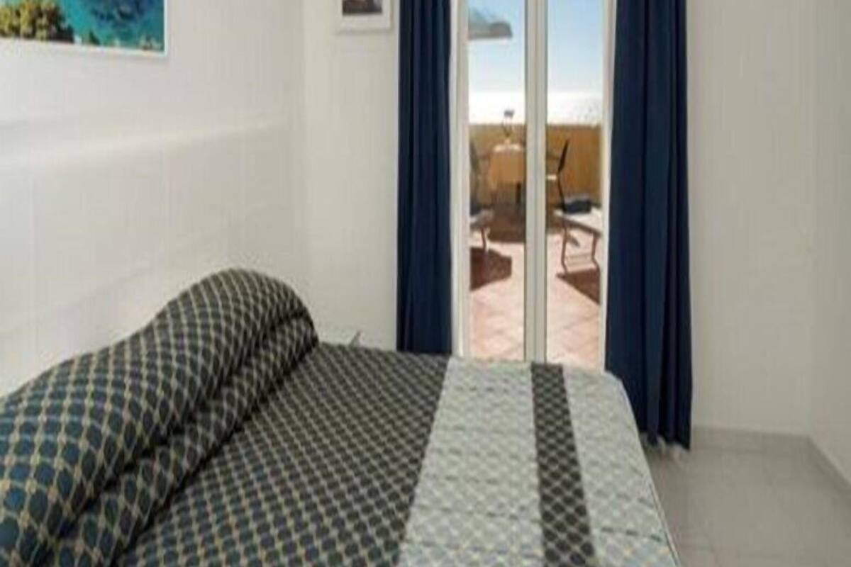 A hotel room with a bed, a painting, a window with curtains, and a view of the outdoors.