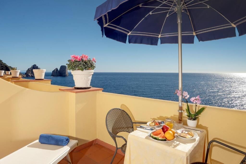 A balcony with a table set for breakfast, overlooking the sea.