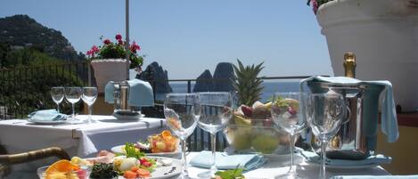 A table set for a meal with various dishes, glasses, and a bottle, overlooking a scenic view.