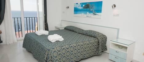 A bedroom with a bed, a nightstand, a glass table, and a painting of a tree by a sea.