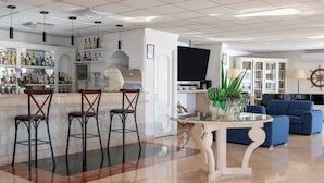A modern bar area with a counter, stools, and a variety of bottles. There is a seating area with a sofa and a table. - Hotel Weber Ambassador (Capri)