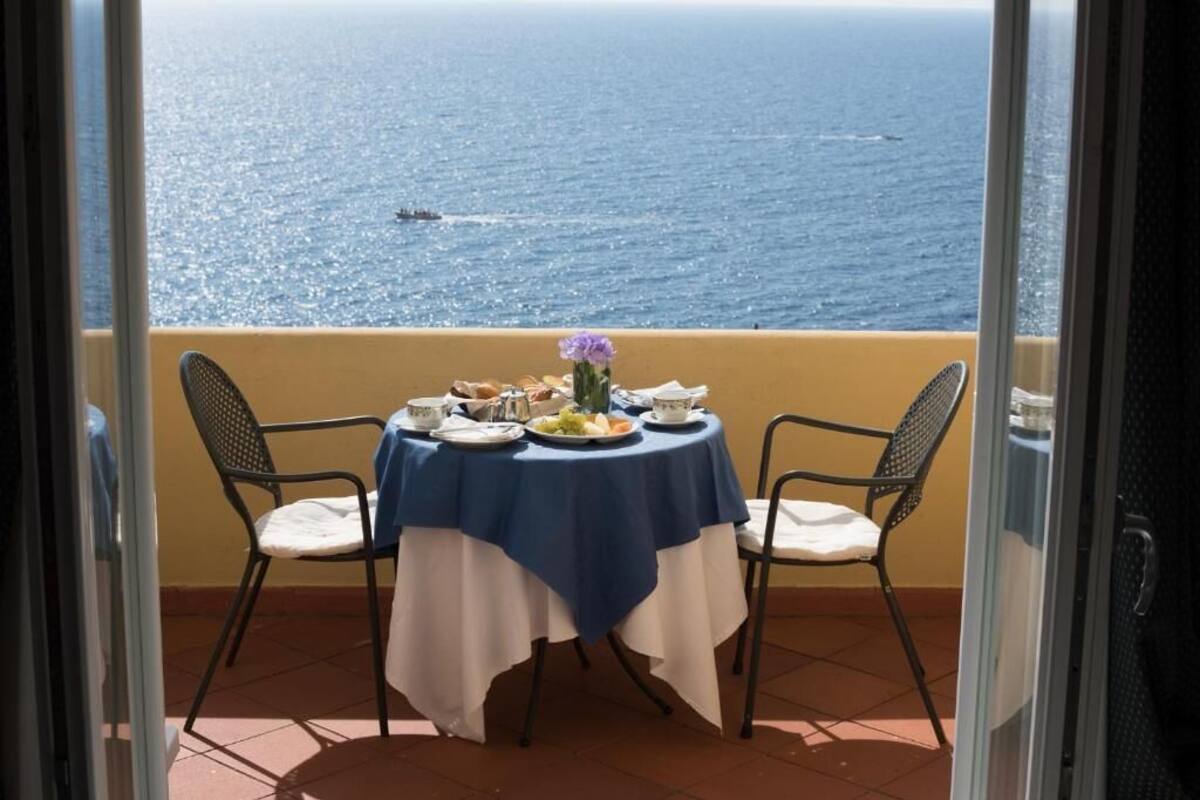 A balcony table with a blue tablecloth, two chairs, and a vase of flowers.