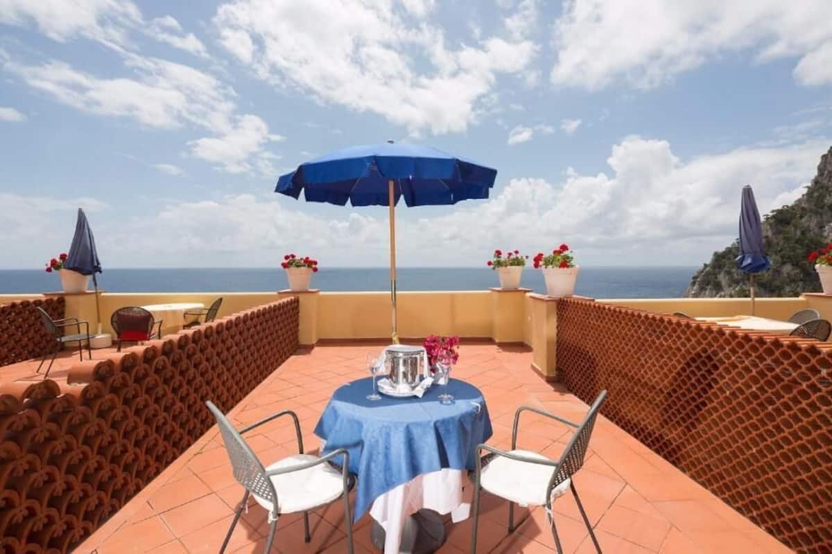 A terrace with a table and chairs, a blue umbrella, and potted plants.