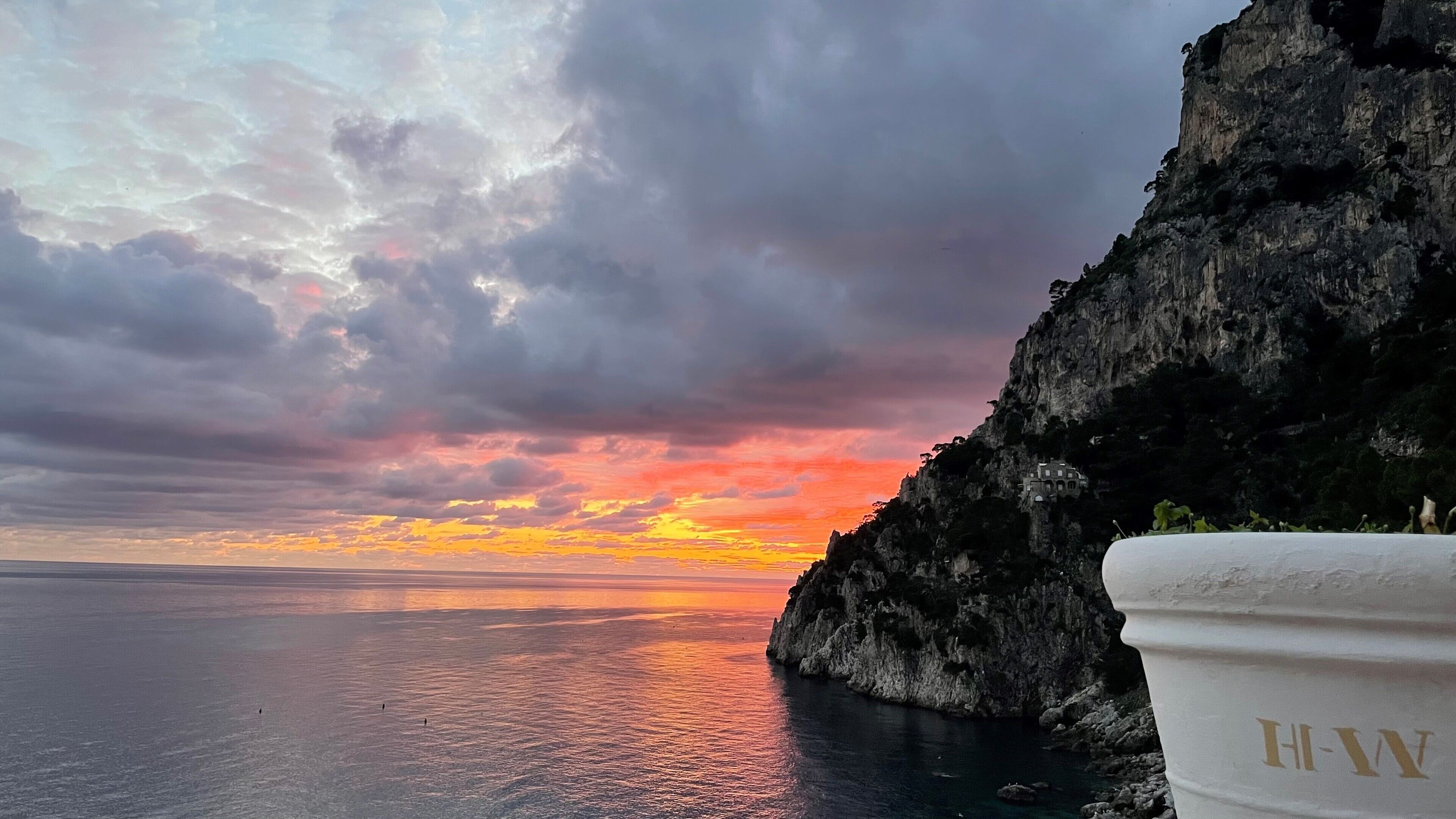 A coastal view with a cliff and a building at sunset.