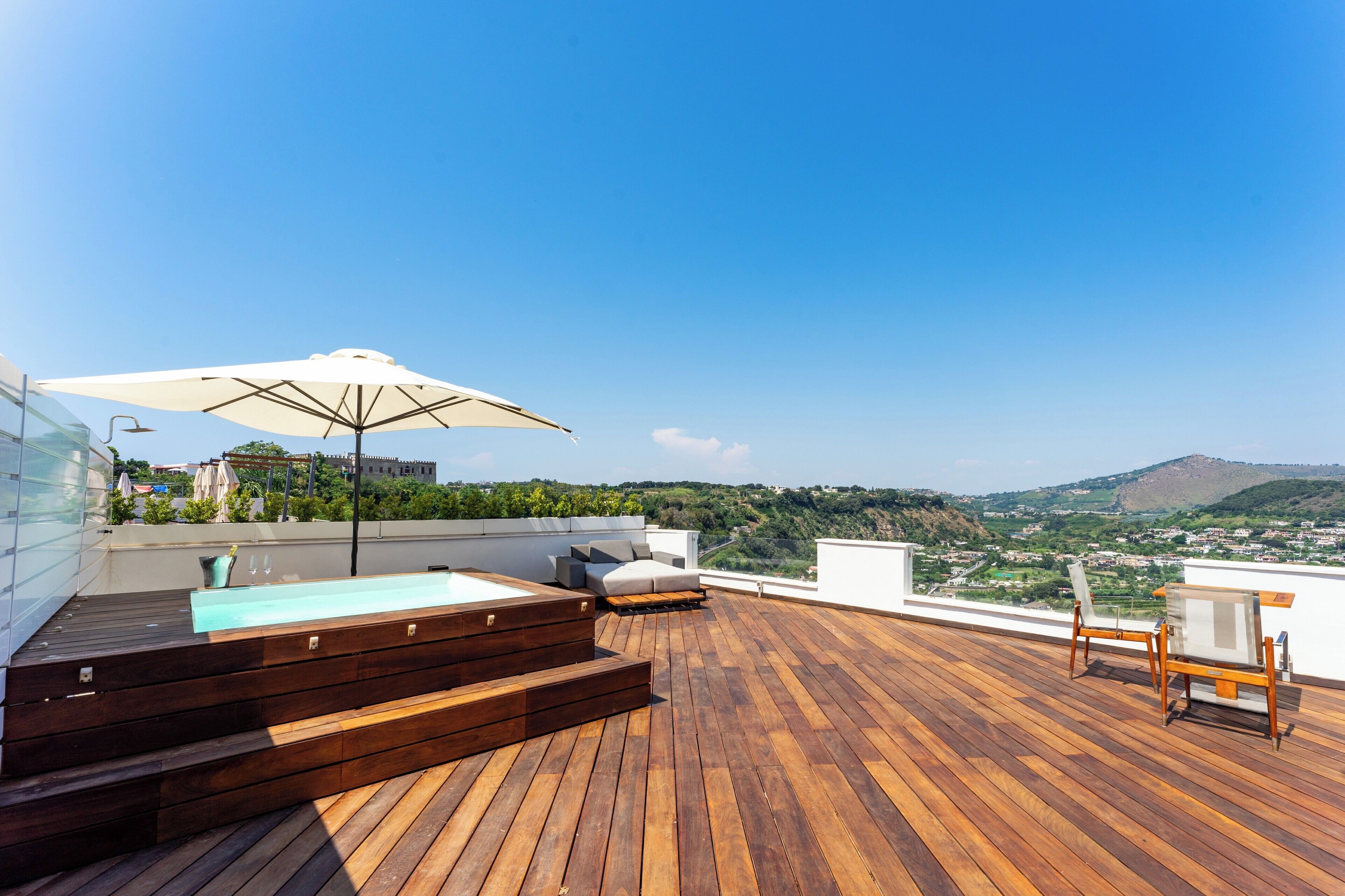 A wooden deck with a hot tub, lounge chairs, and an umbrella.