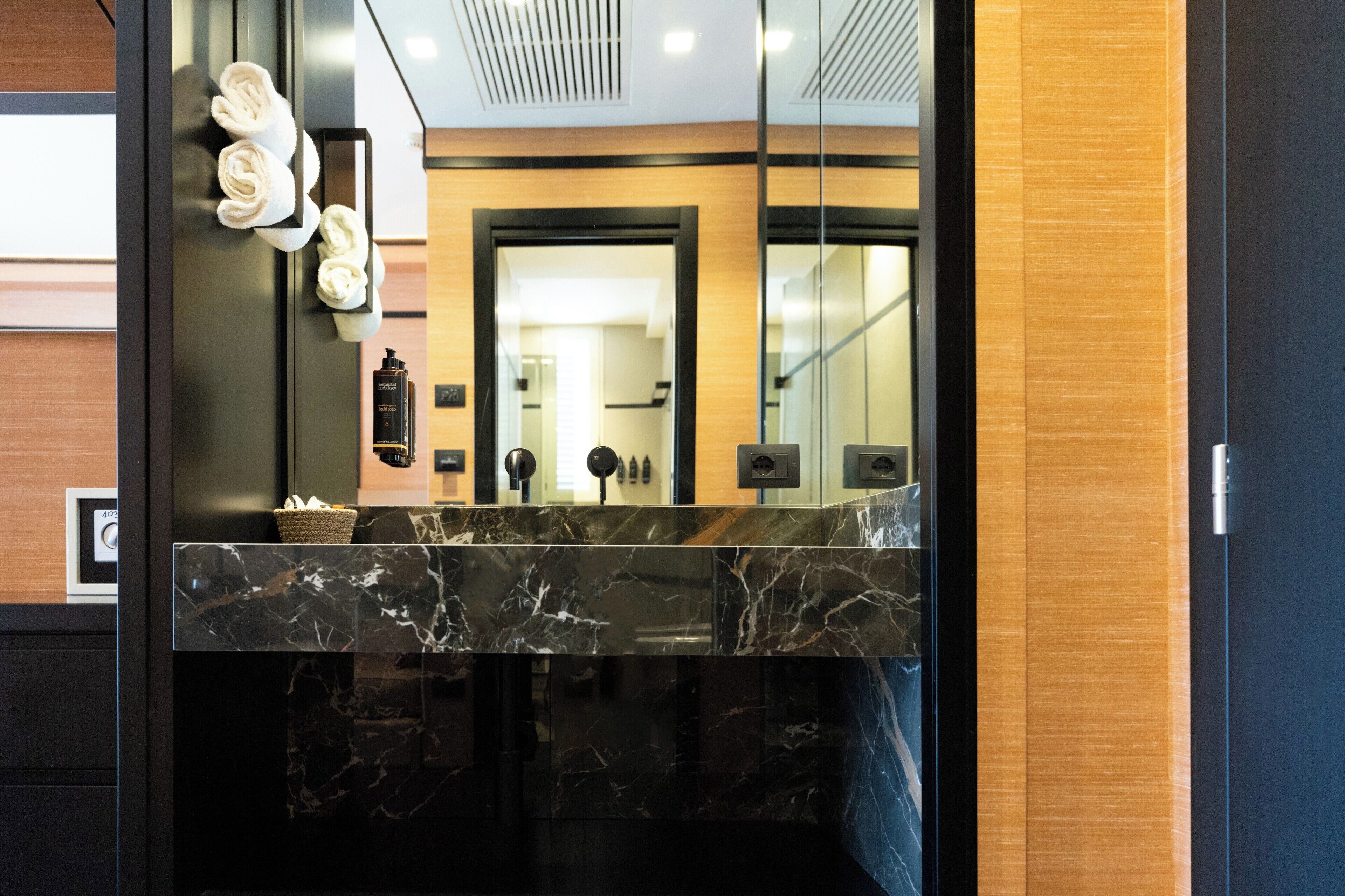 A modern bathroom with a marble countertop, a large mirror, and a wooden panel wall.