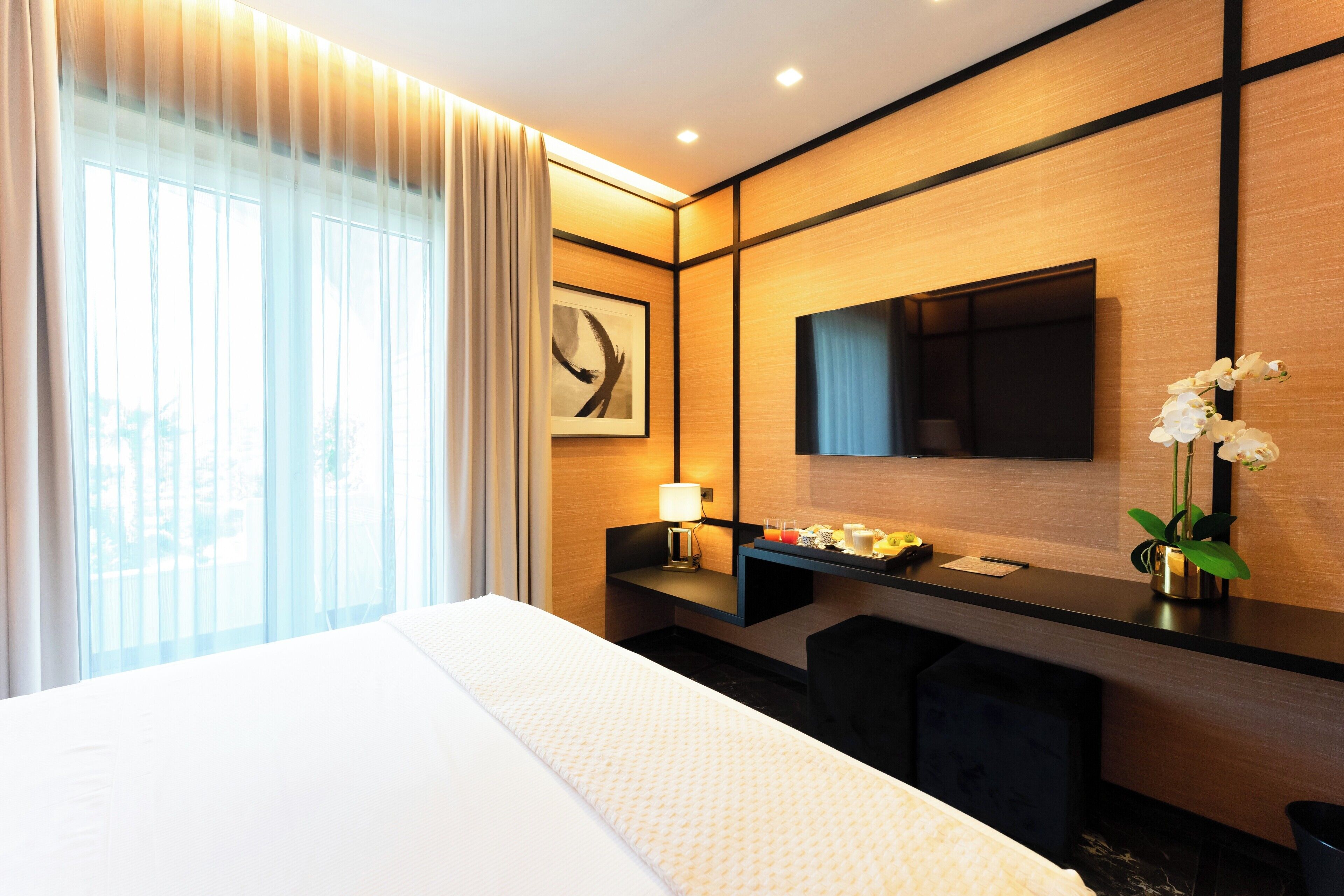 Una habitación de hotel moderna con una cama grande, un escritorio con televisor de pantalla plana, una lámpara de escritorio y un florero con flores.