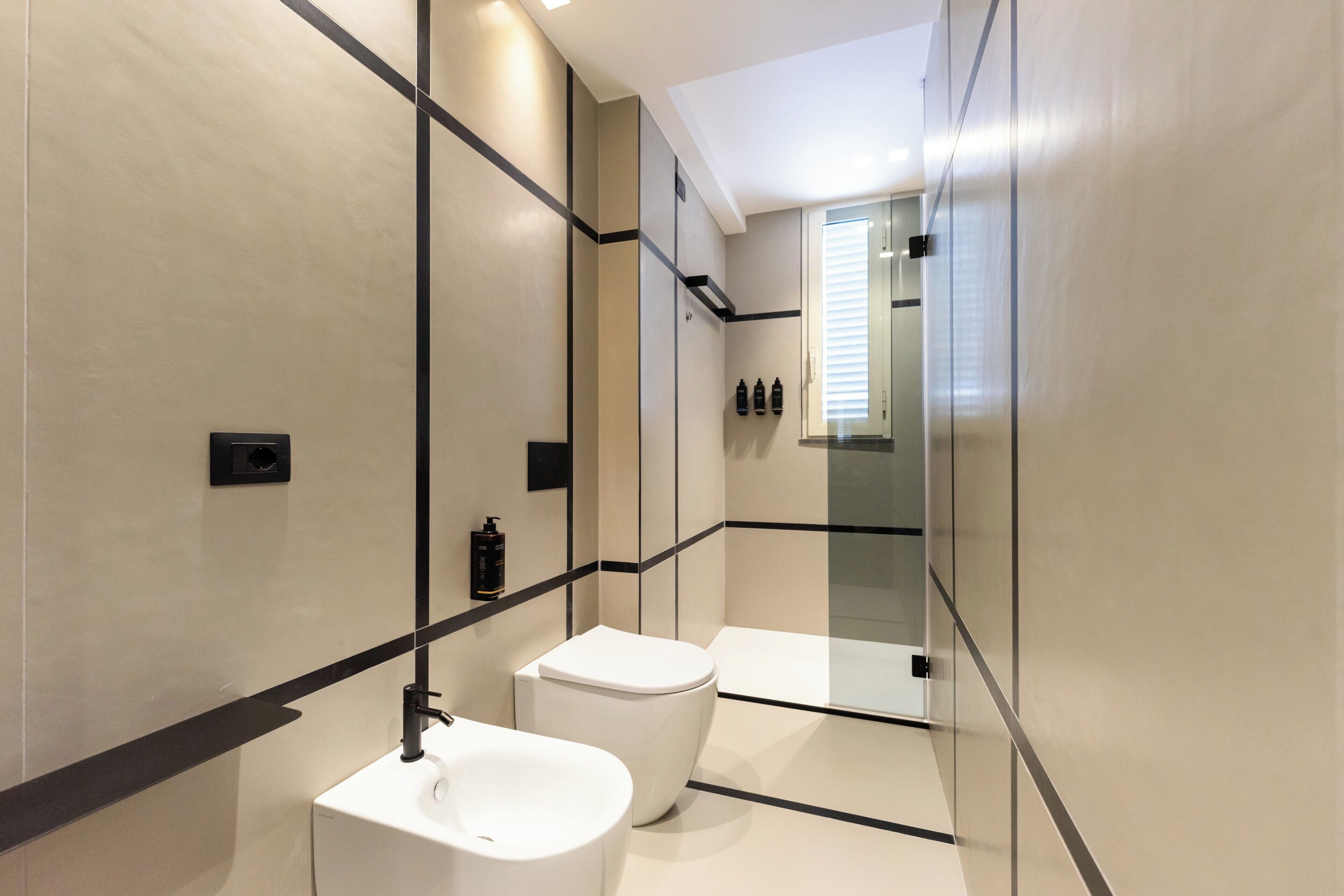 A modern bathroom with a white sink, toilet, and bathtub. There are black lines on the walls and a large mirror.