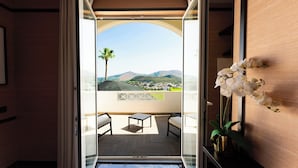 A balcony with a view of a town and mountains, a palm tree, and a vase of white flowers. - Hotel Il Gabbiano (Bacoli)