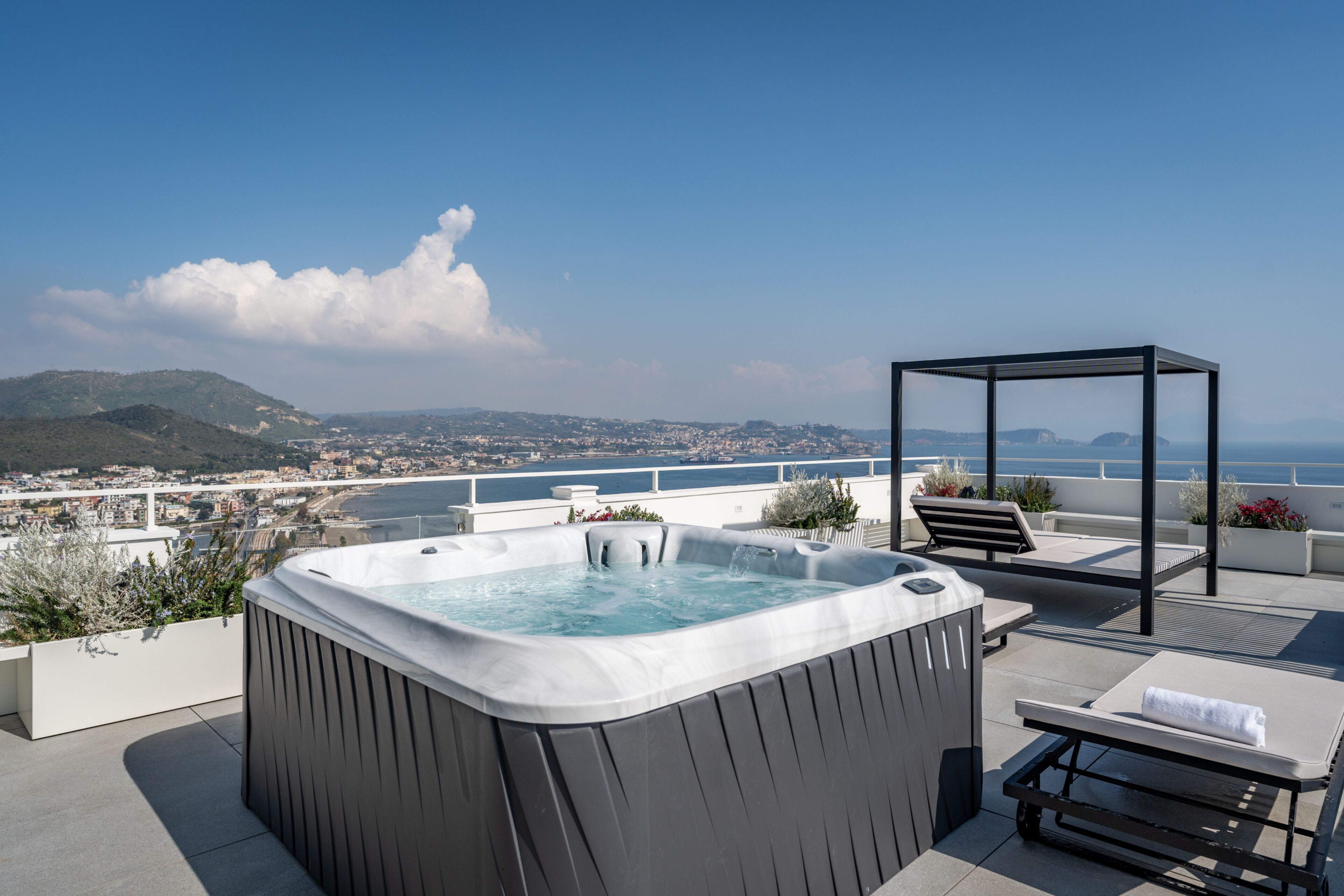 Uma banheira de hidromassagem em um terraço no telhado com vista para a cidade, uma cadeira de descanso e um pérgola.