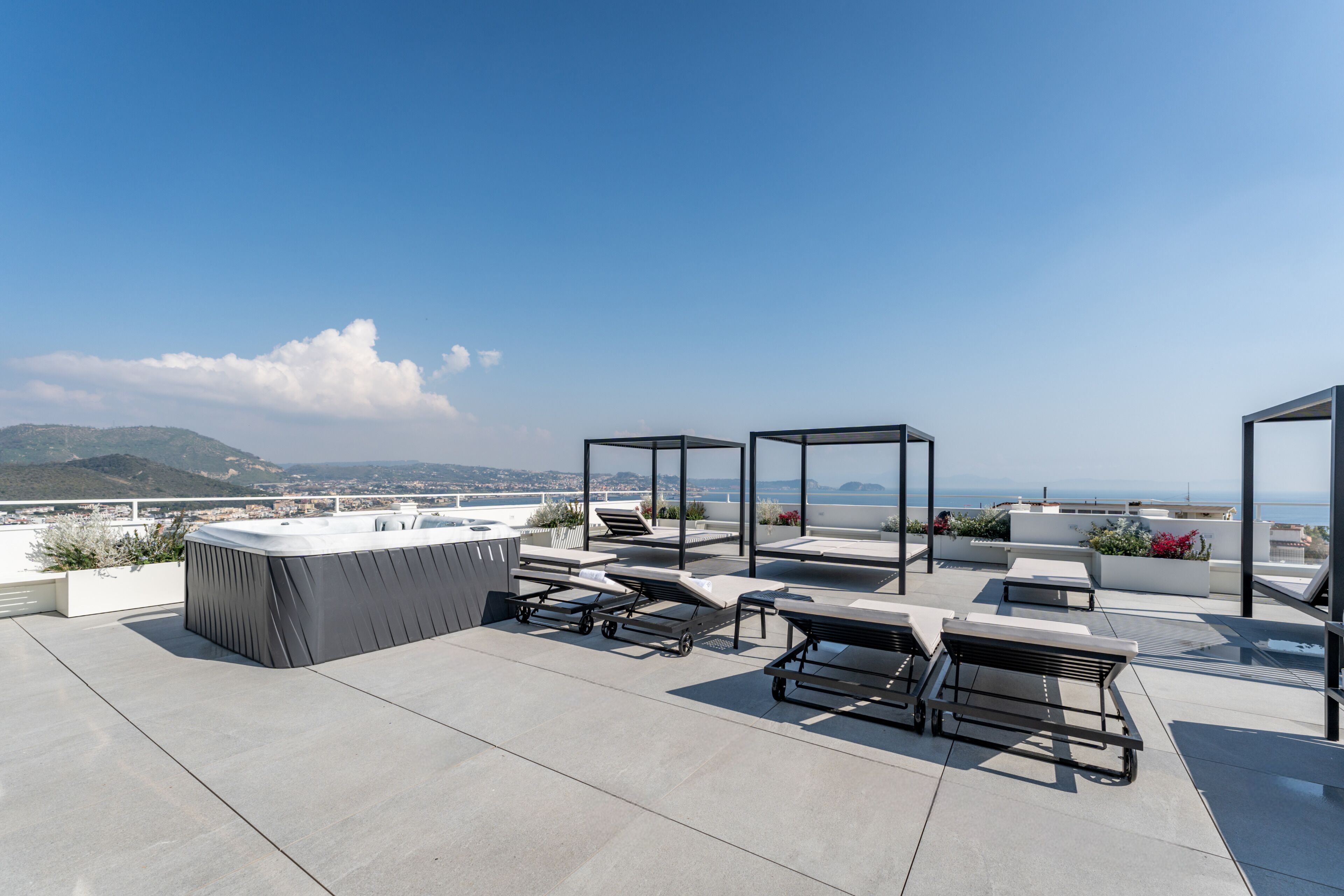 A rooftop terrace with a hot tub, lounge chairs, and a view of the ocean.