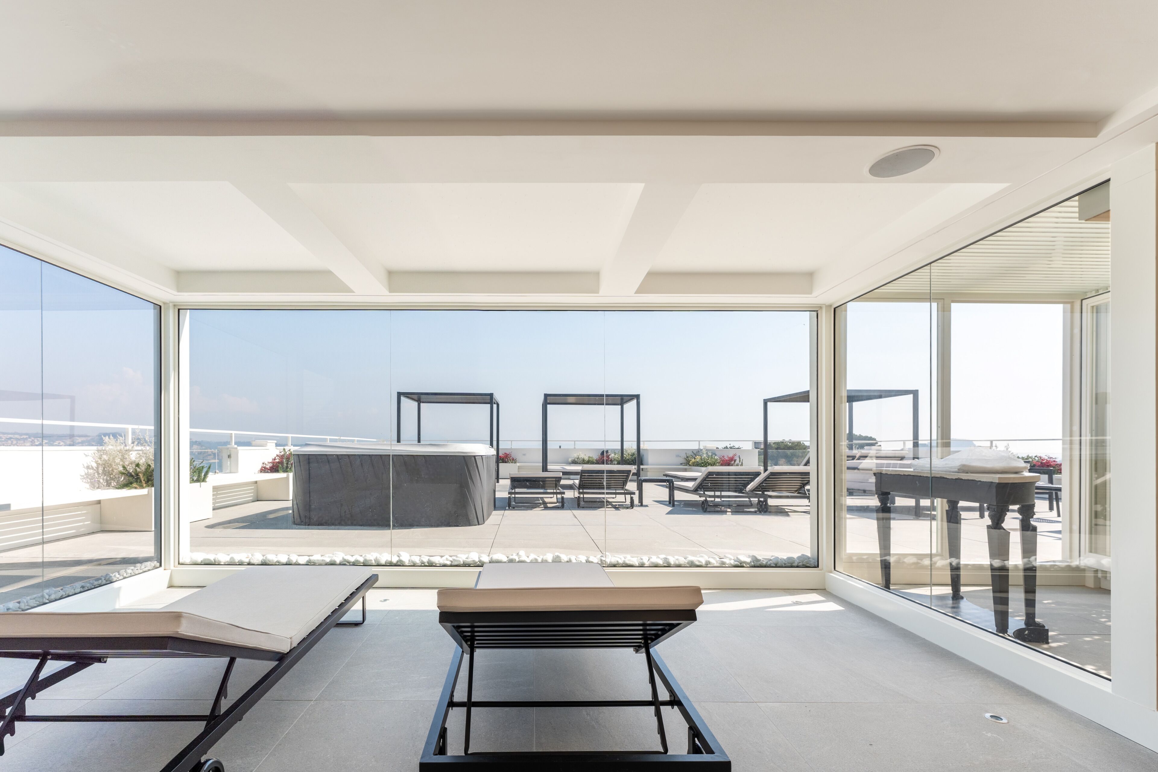 Una terrazza panoramica moderna con parete in vetro, poltrone relax e un tavolo.