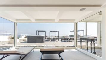 Una terrazza panoramica moderna con parete in vetro, poltrone relax e un tavolo.