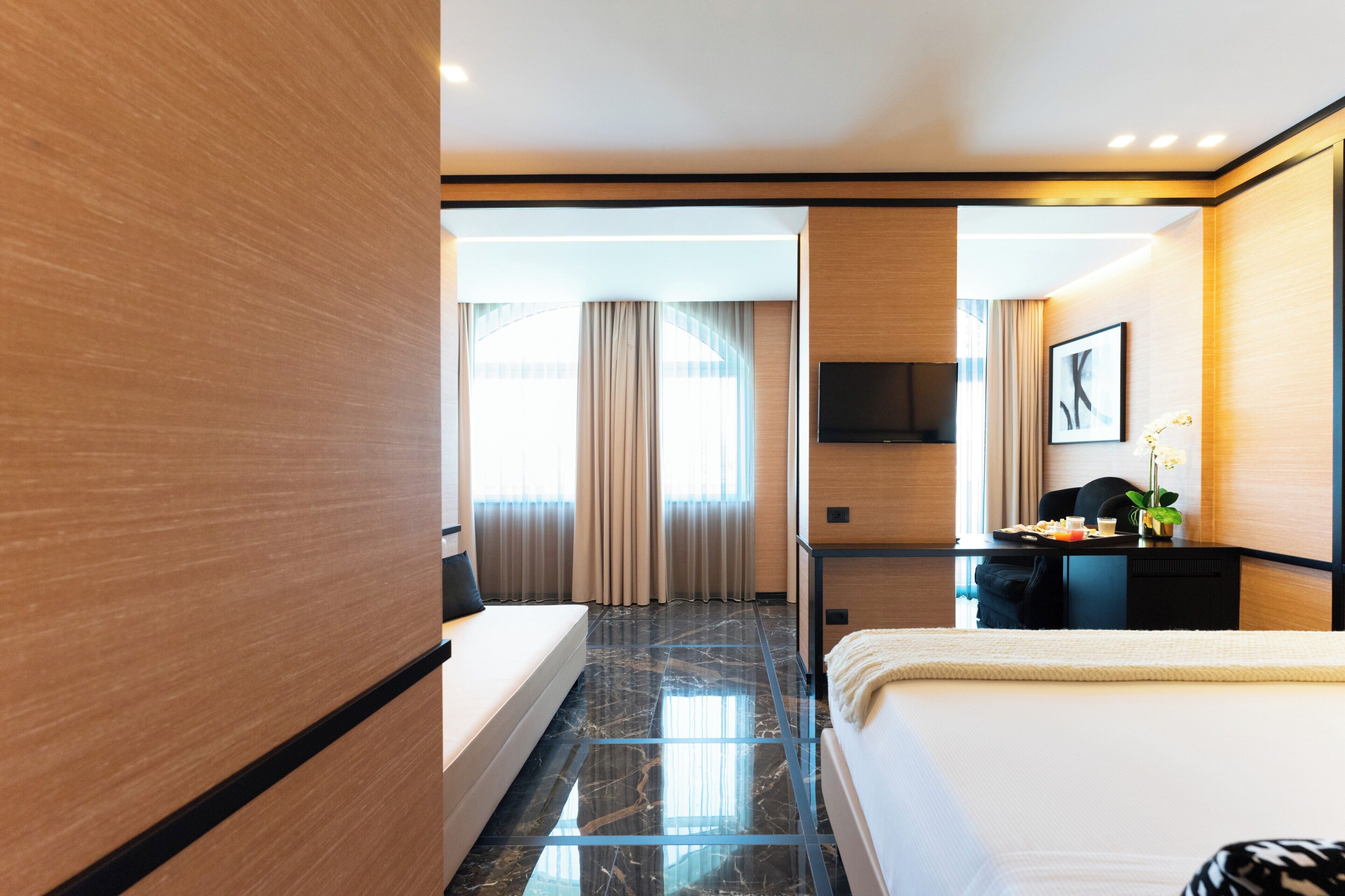 A modern hotel room with a large bed, a desk, a TV, and a view of the outside.