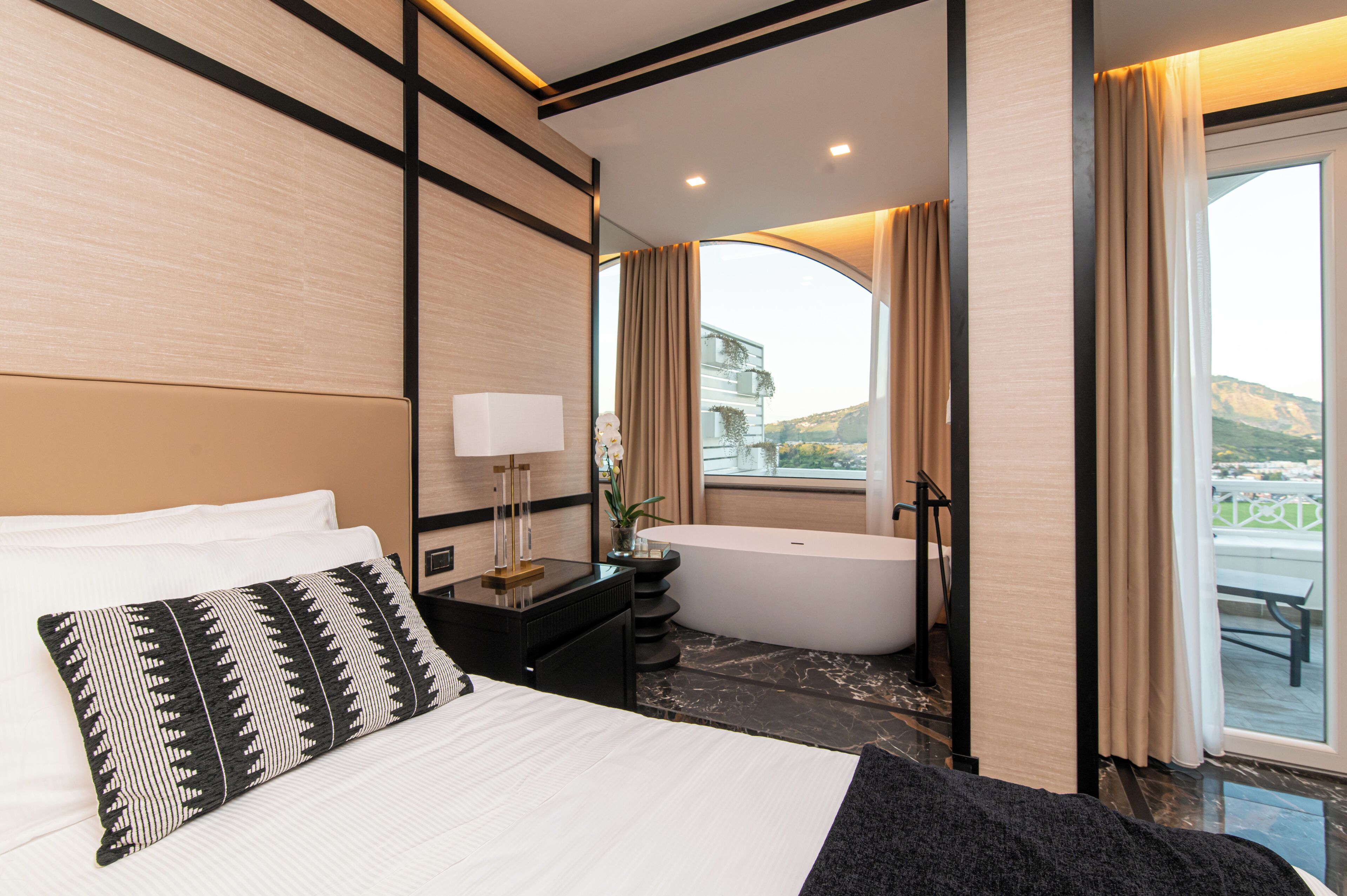 Habitación de hotel moderna con una cama grande, una bañera y vistas al exterior.