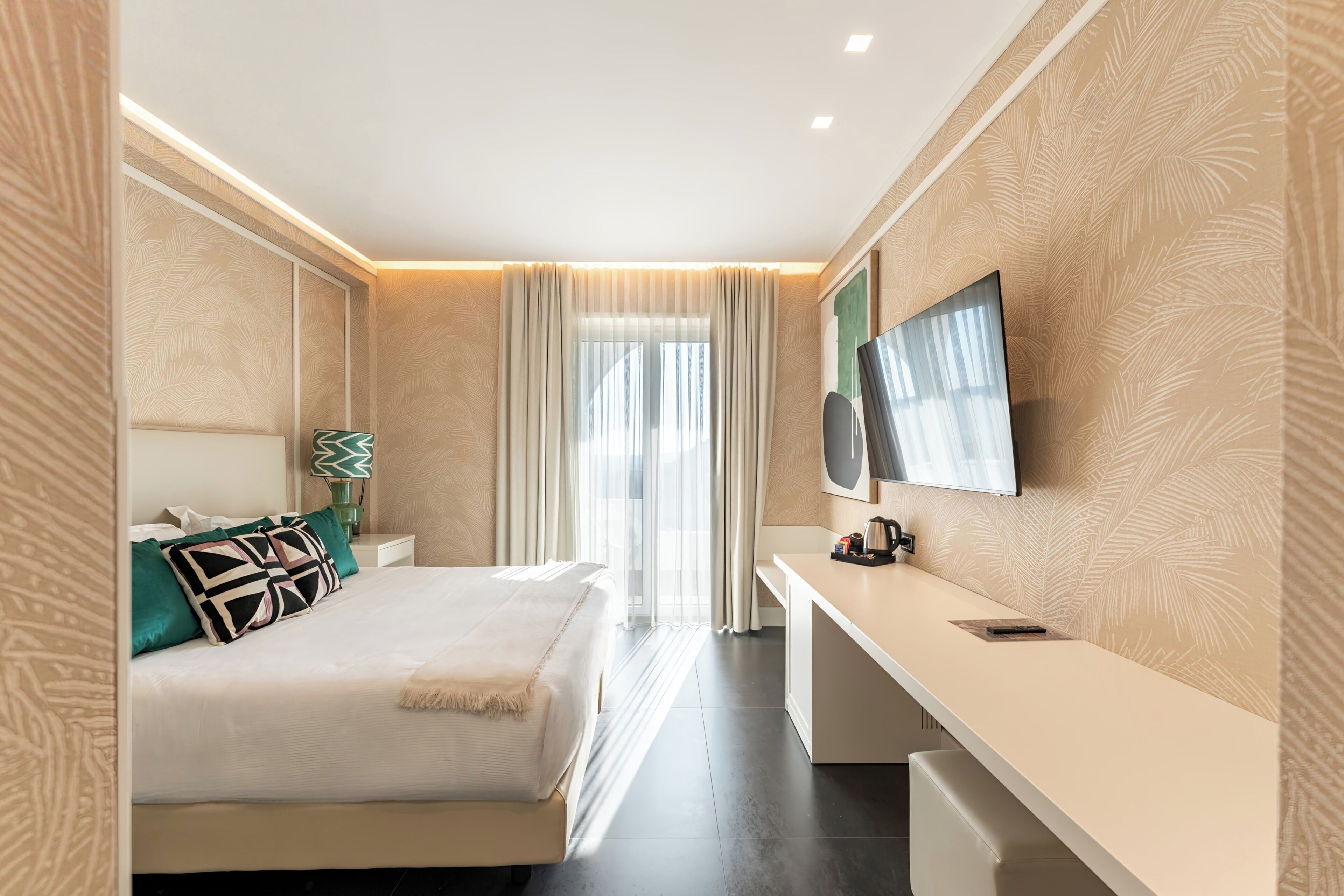 A modern hotel room with a bed, a desk, a television, and a window with curtains.