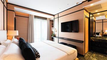 Una habitación de hotel moderna con una cama grande, un televisor de pantalla plana montado en la pared, un baño con encimera de mármol y un ventanal con cortinas.