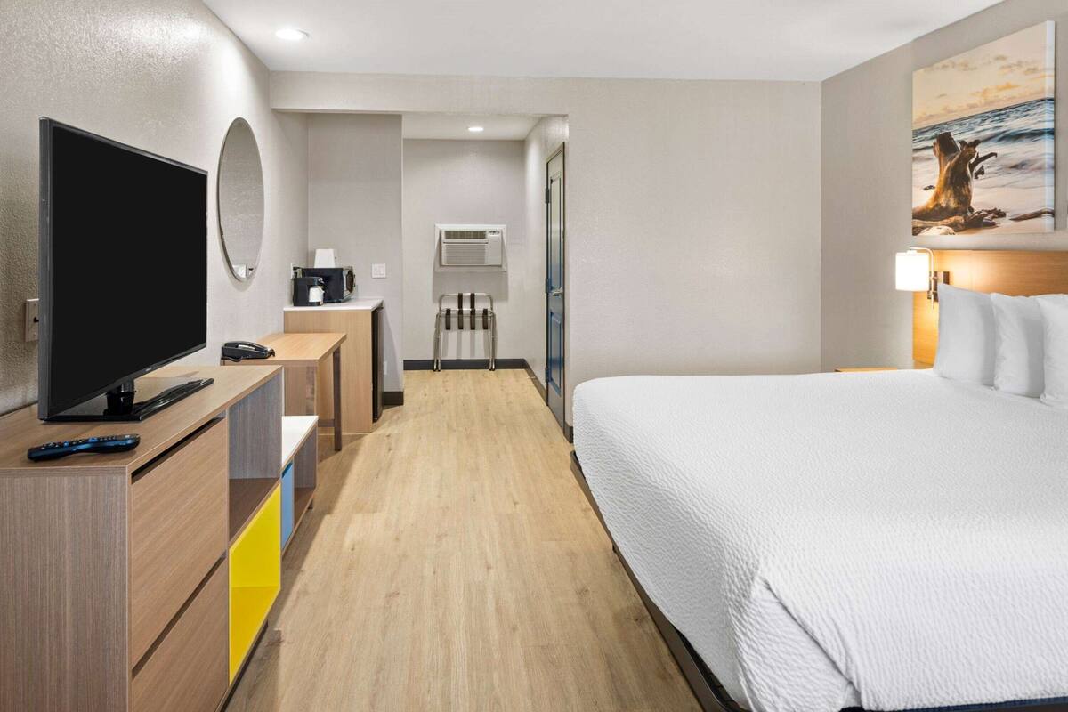 Ein Hotelzimmer mit einem Bett, einem Fernseher, einem Schreibtisch, einem Spiegel, einem Bild und einer Wandklimaanlage.