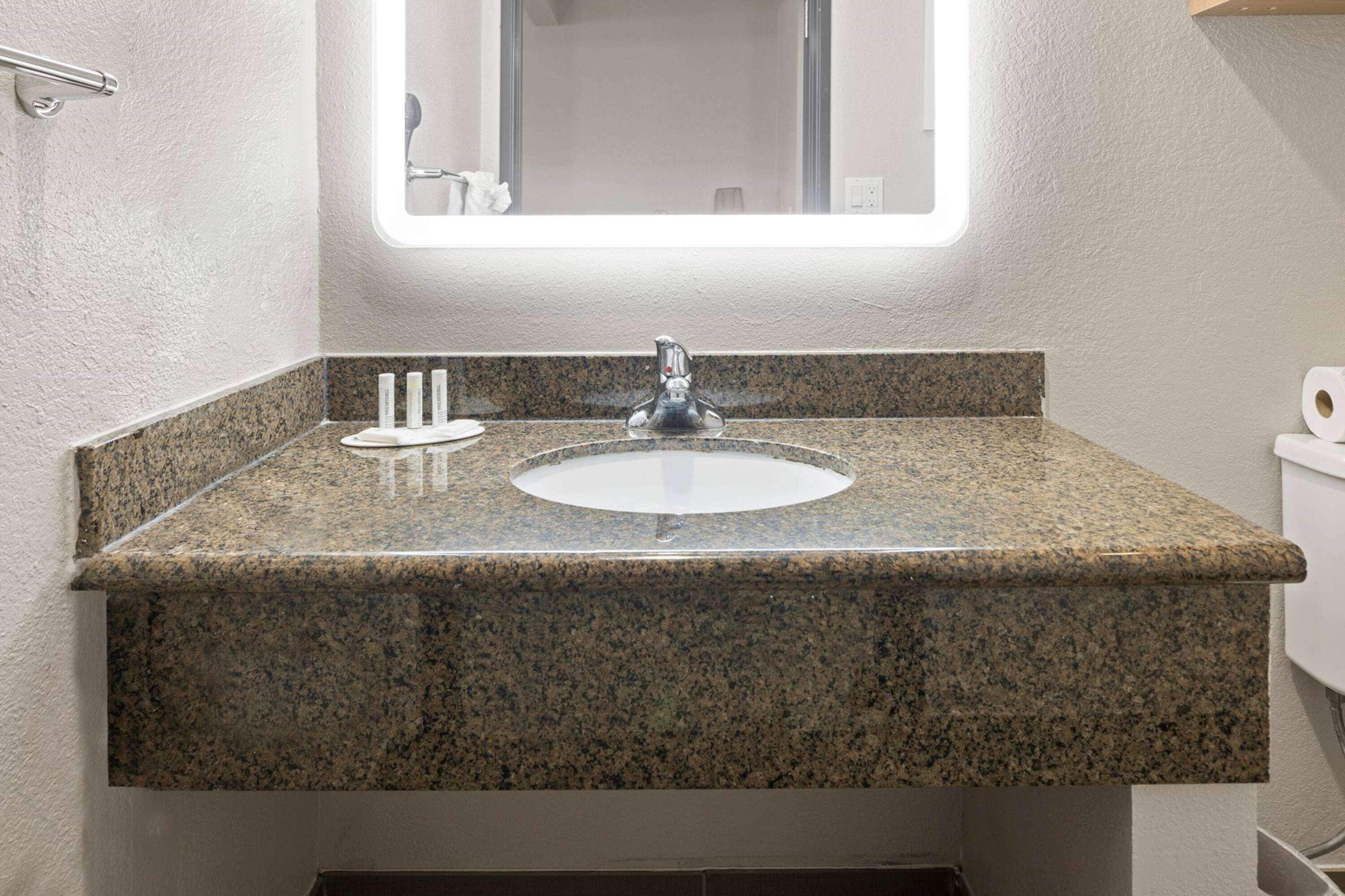 Un baño con encimera de granito, lavamanos y espejo superior.