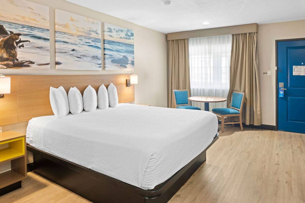 Ein Hotelzimmer mit einem großen Bett, einem kleinen Tisch mit zwei Stühlen, einer blauen Tür und Bildern an der Wand.