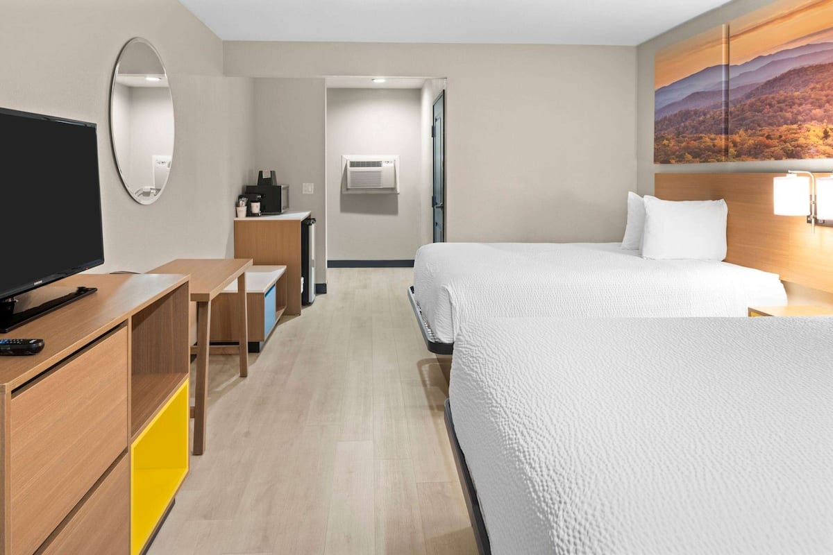 Ein Hotelzimmer mit einem Bett, einem Schreibtisch mit Computer, einem Fernseher und einem Gemälde an der Wand.