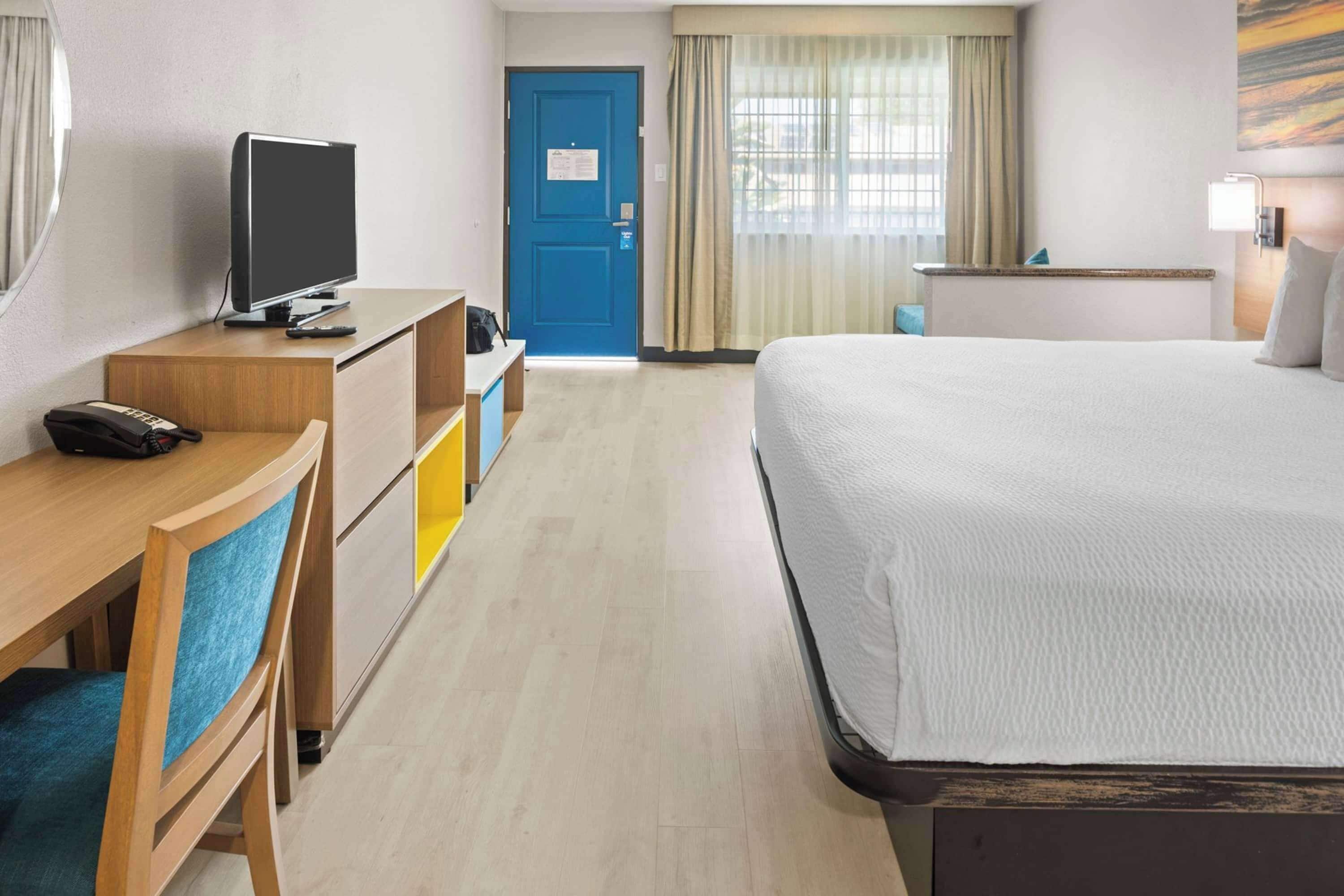 A hotel room with a bed, a desk with a television, a telephone, and a door.