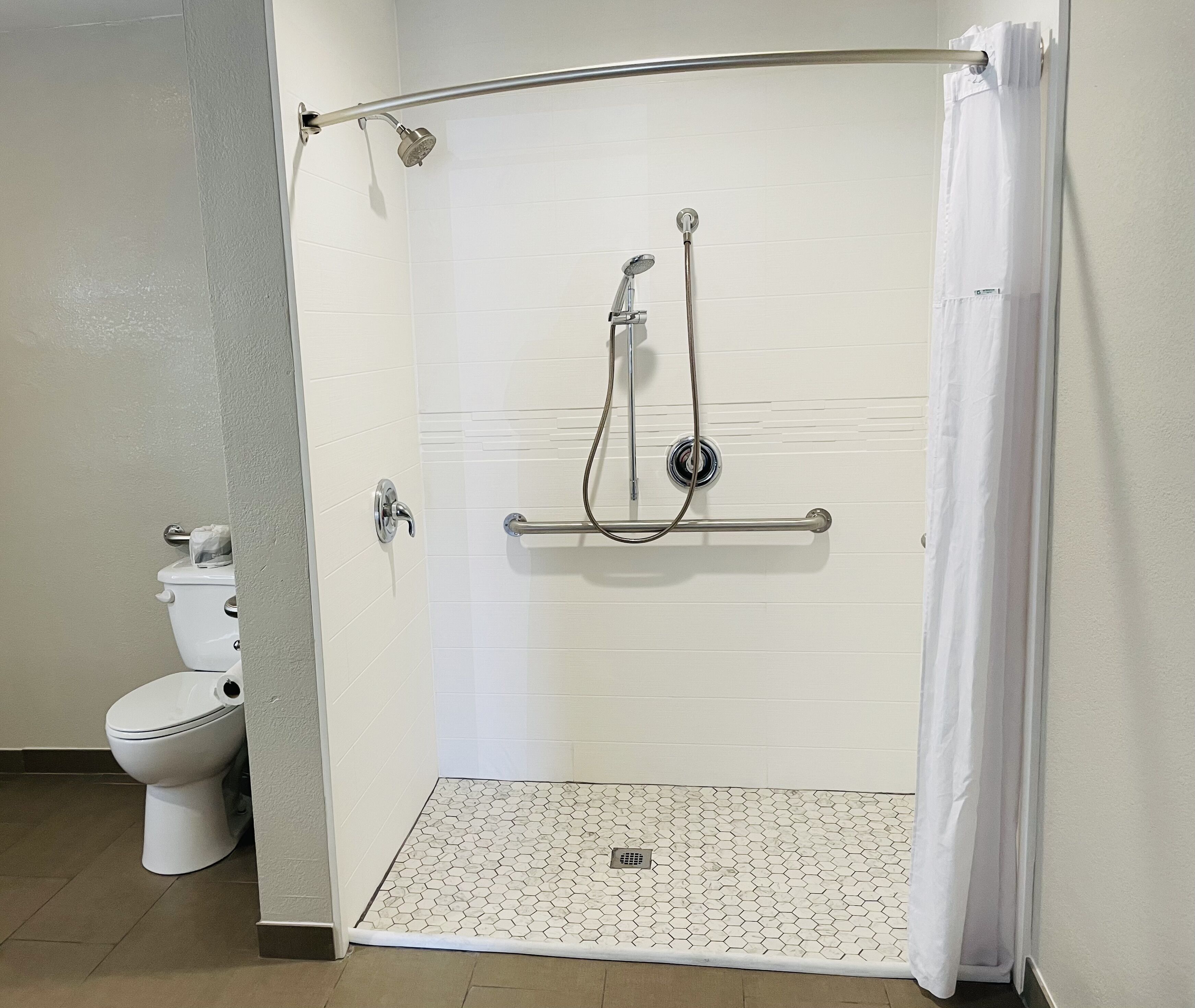 A shower area with a white tiled wall, a grab bar, and a white toilet.