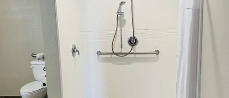 A shower area with a white tiled wall, a grab bar, and a white toilet.