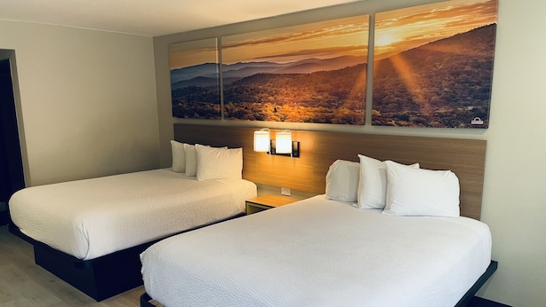 A hotel room with two beds, a large landscape painting above the beds, and a nightstand with a lamp. - Days Inn by Wyndham San Diego-East/El Cajon (El Cajon)