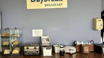 A breakfast counter with a sign reading "Daybreak Breakfast," a coffee machine, a toaster, and a display case with pastries.
