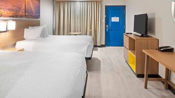 Ein Hotelzimmer mit zwei Betten, einem Fernseher, einem Schreibtisch und einem kleinen Tisch.