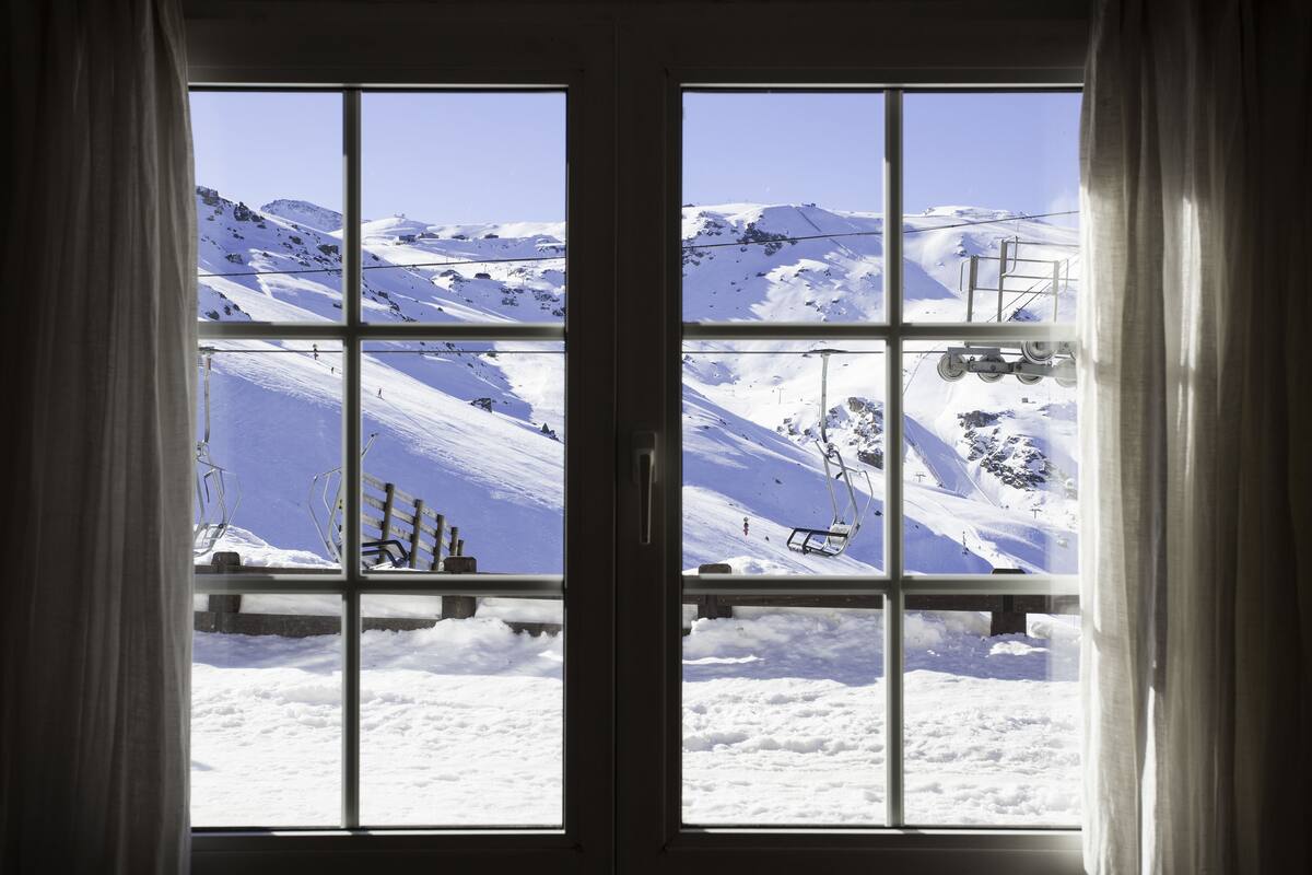 Ventana con vistas a un paisaje montañoso nevado, incluyendo pistas de esquí y un telesilla.