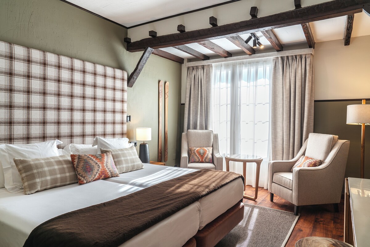 A hotel room with a large bed, two armchairs, a small table, and a window with curtains.