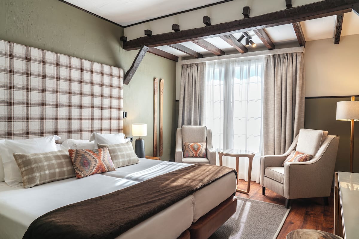 Habitación de hotel con una cama grande, dos sillones, una mesita y vistas al exterior a través de amplios ventanales.