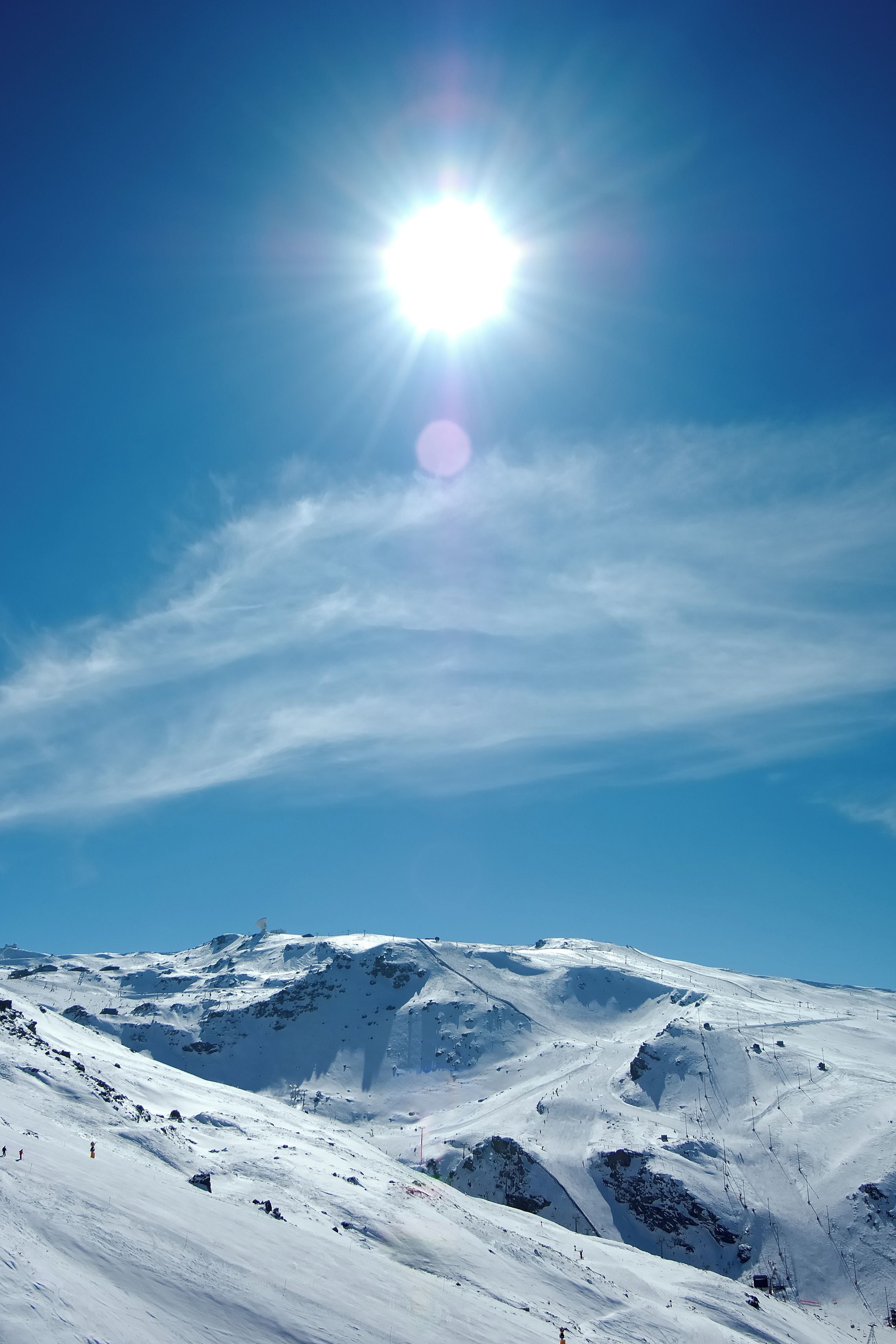 Paisaje montañoso nevado con cielos despejados y un sol brillante.