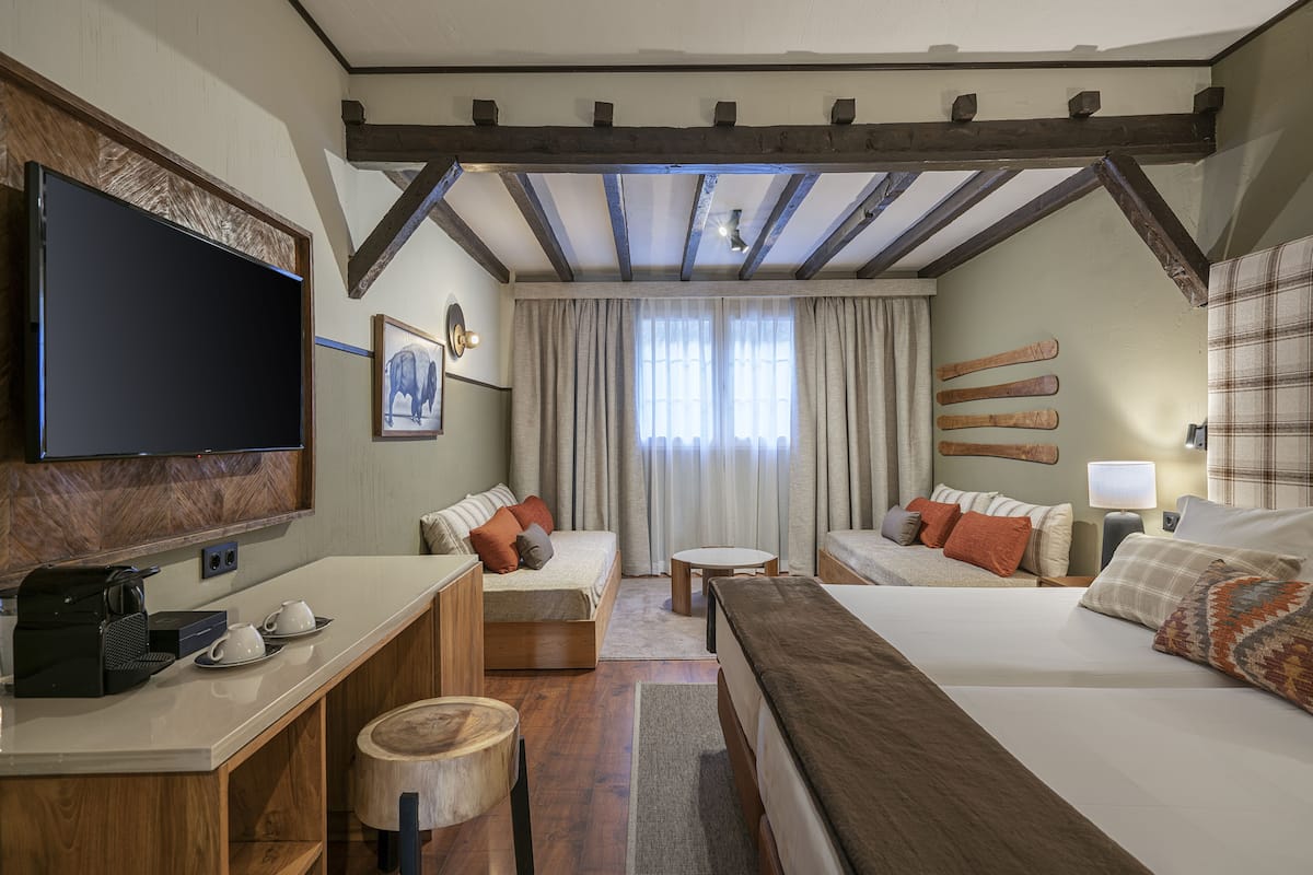 Habitación de hotel con una cama grande, un sofá, un escritorio con cafetera, televisor y vigas de madera en el techo.